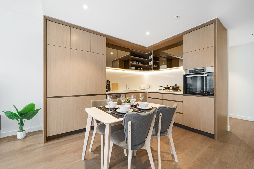 Photo of a contemporary open plan kitchen in Sydney with an undermount sink, flat-panel cabinets, brown cabinets, white splashback, panelled appliances, medium hardwood floors, no island, brown floor and white benchtop.