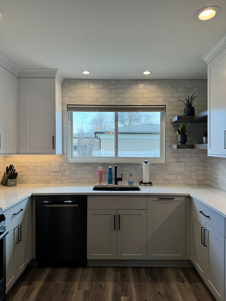 Photo of a medium sized traditional u-shaped kitchen/diner in Detroit with a single-bowl sink, shaker cabinets, white cabinets, engineered stone countertops, white splashback, ceramic splashback, black appliances, vinyl flooring, no island, brown floors and white worktops.