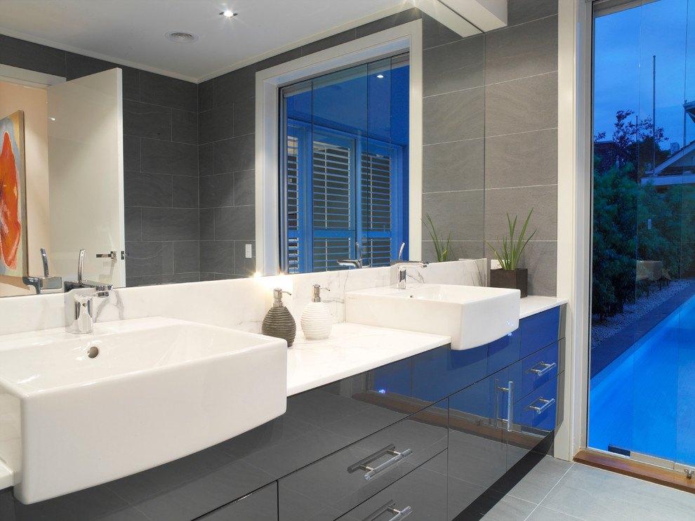 Photo of a mid-sized contemporary master bathroom in Melbourne with a vessel sink, flat-panel cabinets, grey cabinets, marble benchtops, a shower/bathtub combo, a one-piece toilet, gray tile, porcelain tile, grey walls and porcelain floors.