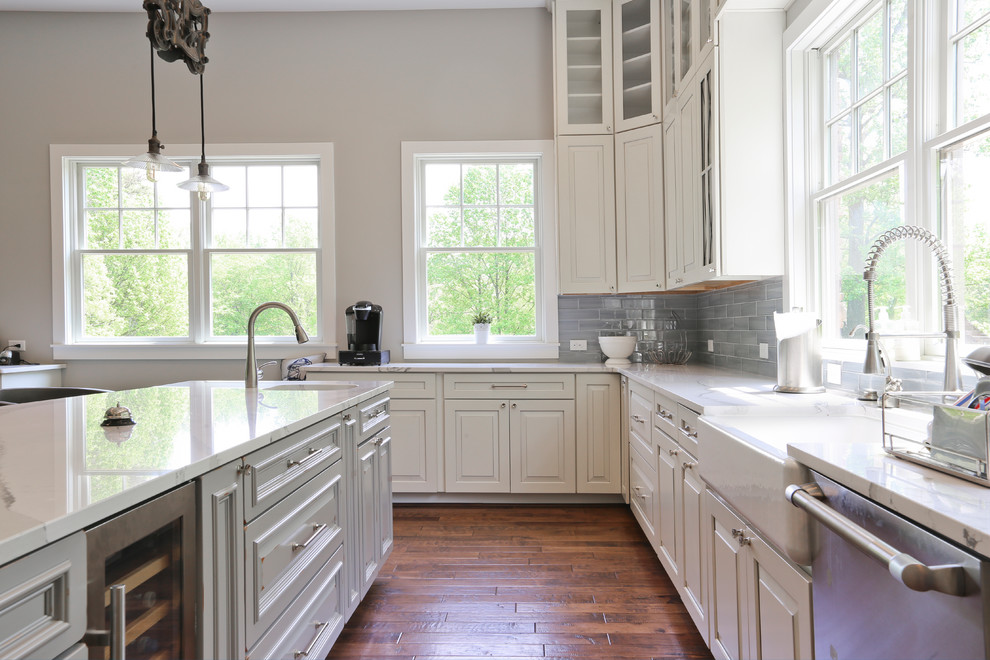 Photo of an expansive country u-shaped open plan kitchen in DC Metro with a farmhouse sink, raised-panel cabinets, white cabinets, quartz benchtops, grey splashback, porcelain splashback, stainless steel appliances, dark hardwood floors, with island and brown floor.