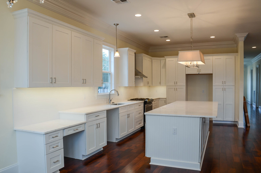 This is an example of a mid-sized traditional l-shaped open plan kitchen in New Orleans with an undermount sink, flat-panel cabinets, white cabinets, white splashback, subway tile splashback, stainless steel appliances, dark hardwood floors and with island.