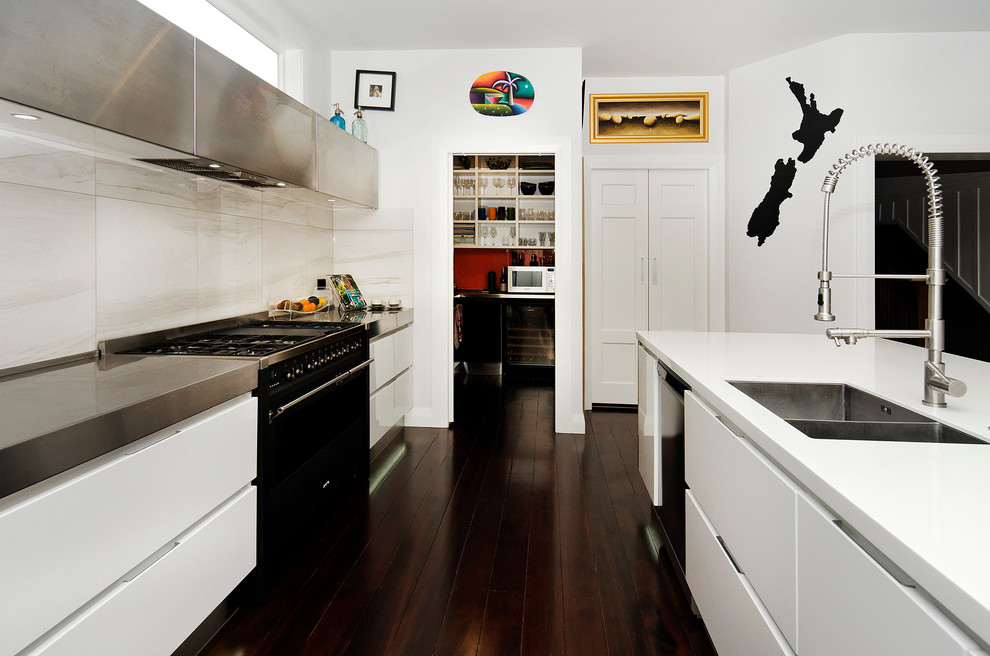 Inspiration for a mid-sized contemporary galley eat-in kitchen in Auckland with an undermount sink, flat-panel cabinets, black cabinets, solid surface benchtops, grey splashback, stone tile splashback, black appliances, dark hardwood floors and with island.