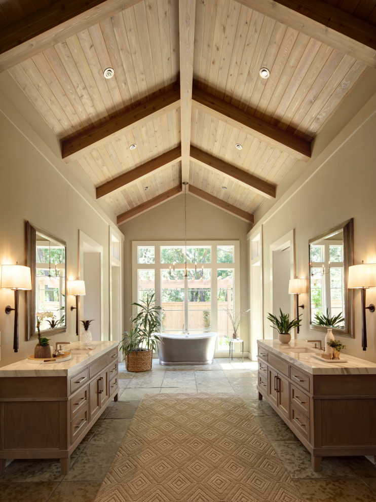 Country master bathroom in San Francisco with a freestanding tub, beige walls, limestone floors, a freestanding vanity, exposed beam, vaulted, wood, beaded inset cabinets, medium wood cabinets, an undermount sink, grey floor, white benchtops and a double vanity.