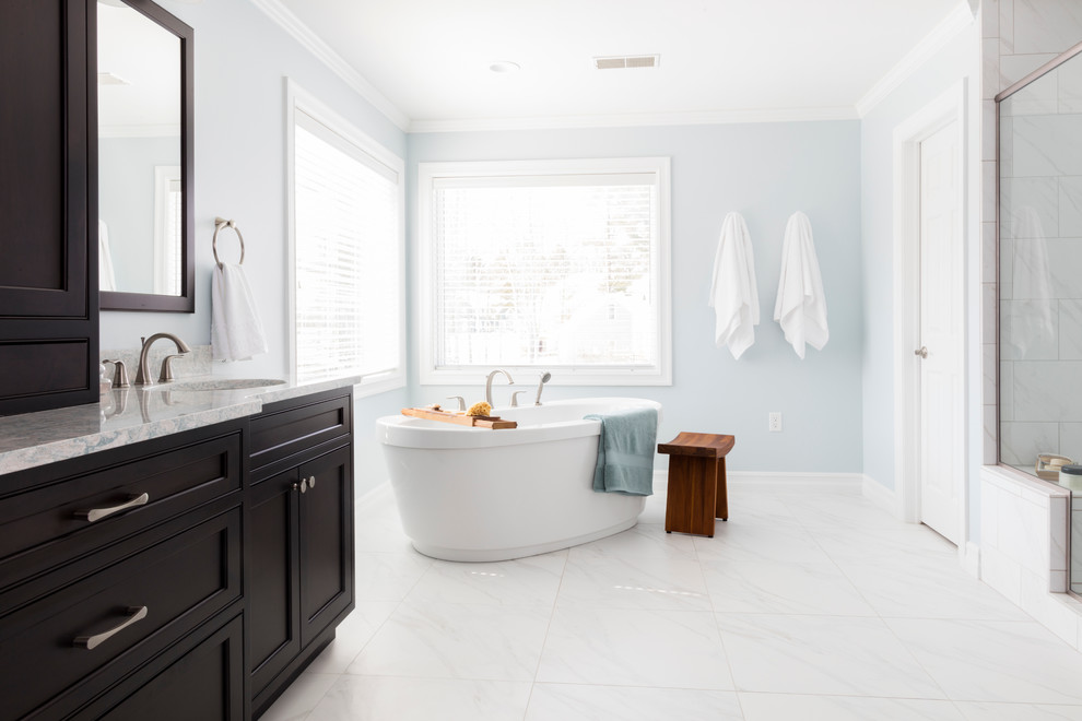 Photo of a transitional master bathroom in New York with beaded inset cabinets, dark wood cabinets, a freestanding tub, a two-piece toilet, white tile, porcelain tile, blue walls, porcelain floors, an undermount sink and engineered quartz benchtops.