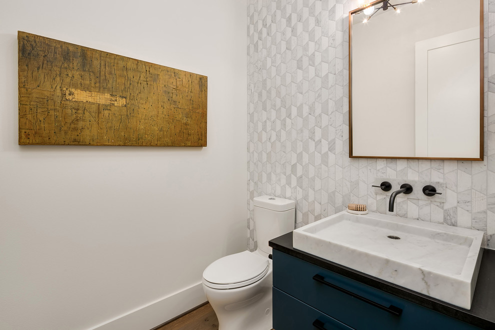 Large contemporary powder room in Seattle with flat-panel cabinets, blue cabinets, a two-piece toilet, gray tile, marble, white walls, medium hardwood floors, a vessel sink, grey floor and black benchtops.