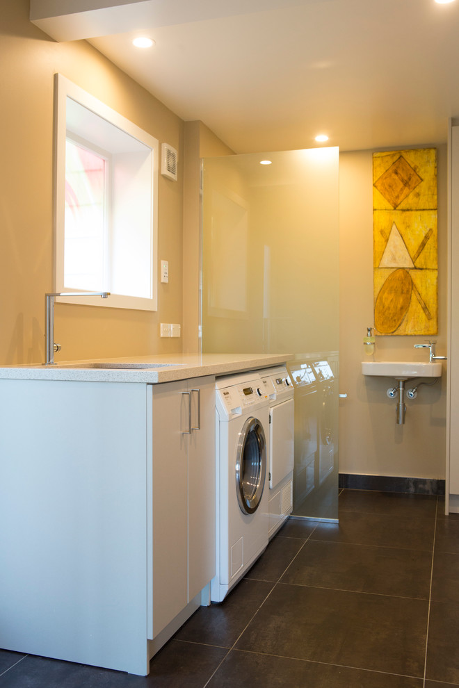 Photo of a large contemporary u-shaped utility room in Auckland with an undermount sink, flat-panel cabinets, laminate benchtops, beige walls, ceramic floors, a side-by-side washer and dryer and white cabinets.