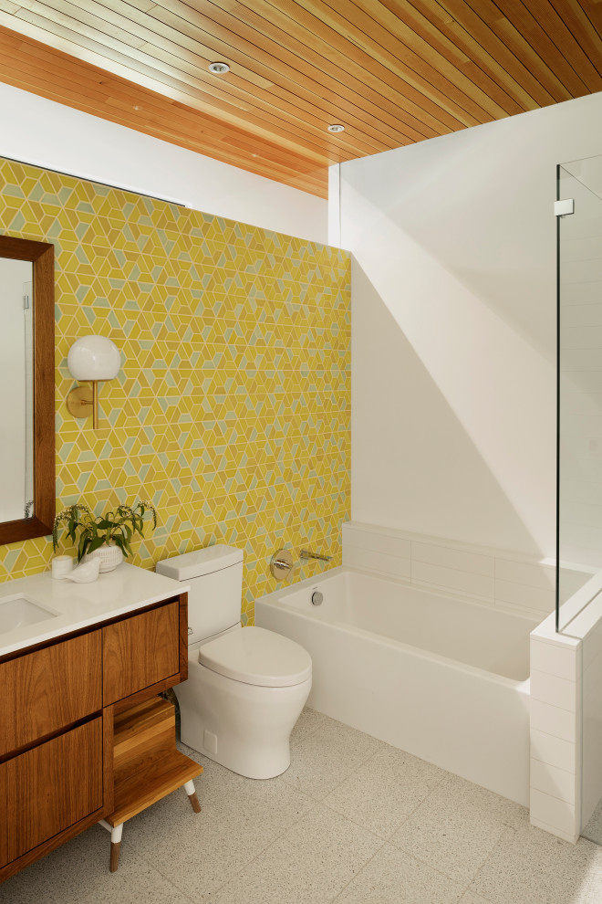 Photo of a medium sized retro family bathroom in Portland with medium wood cabinets, an alcove bath, a built-in shower, a two-piece toilet, multi-coloured tiles, ceramic tiles, white walls, terrazzo flooring, a submerged sink, engineered stone worktops, white floors, a hinged door, white worktops, a single sink, a floating vanity unit, a vaulted ceiling and flat-panel cabinets.