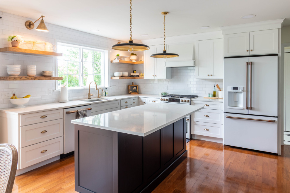 Mid-sized transitional l-shaped medium tone wood floor and brown floor open concept kitchen photo in Other with an undermount sink, shaker cabinets, white cabinets, quartzite countertops, white backsplash, ceramic backsplash, white appliances, an island and white countertops