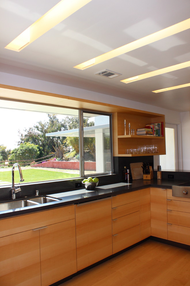 This is an example of a mid-sized contemporary u-shaped open plan kitchen in San Diego with a double-bowl sink, flat-panel cabinets, light wood cabinets, quartz benchtops, window splashback, panelled appliances, light hardwood floors, a peninsula and beige floor.