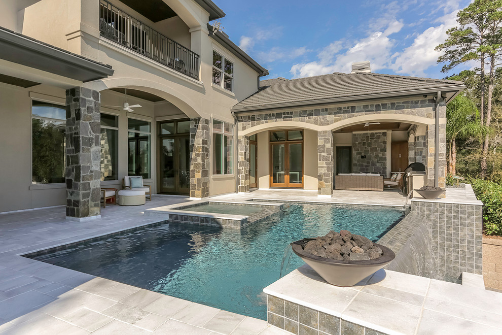 This is an example of a mid-sized traditional backyard rectangular infinity pool in Houston with natural stone pavers and a hot tub.