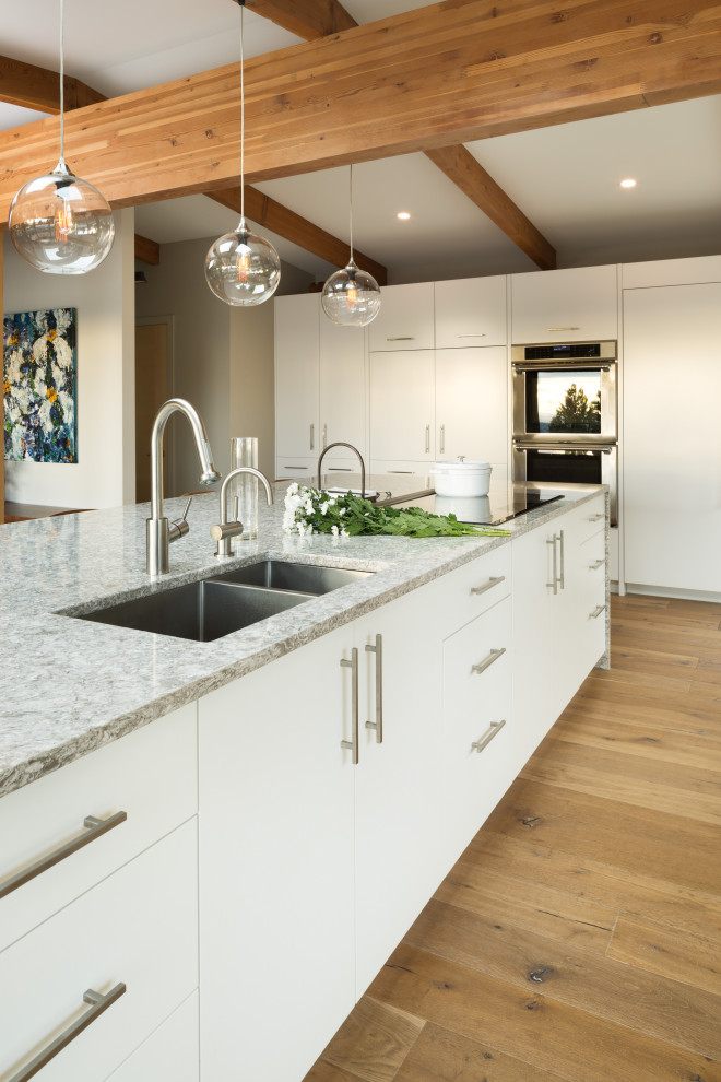 This is an example of a large contemporary l-shaped eat-in kitchen in Vancouver with an undermount sink, flat-panel cabinets, white cabinets, quartzite benchtops, stainless steel appliances, laminate floors, with island, brown floor and multi-coloured benchtop.