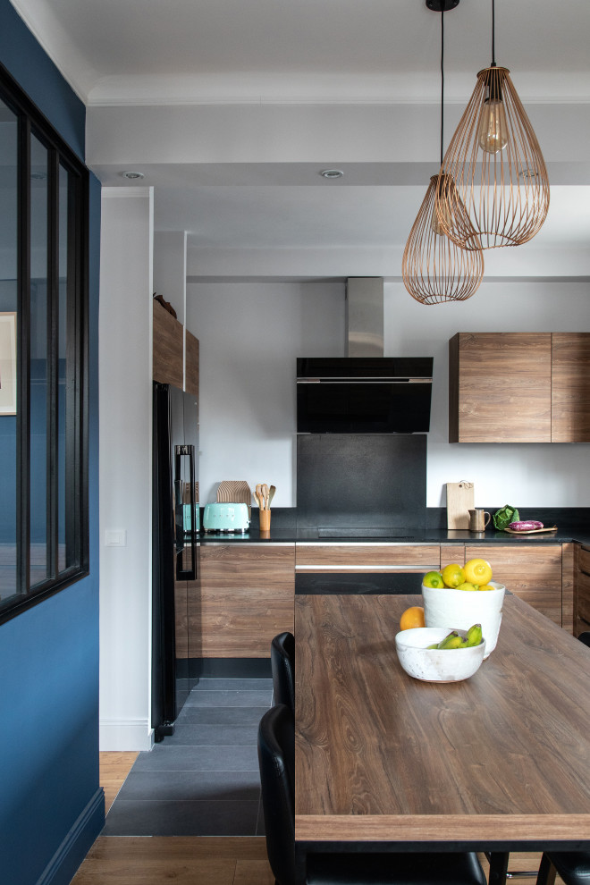 Inspiration for a mid-sized contemporary l-shaped eat-in kitchen in Paris with an undermount sink, medium wood cabinets, granite benchtops, black splashback, granite splashback, ceramic floors, with island, black floor and black benchtop.