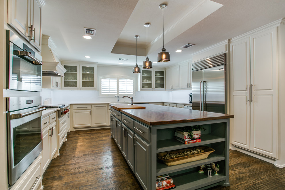 This is an example of a large transitional u-shaped eat-in kitchen in Dallas with a farmhouse sink, raised-panel cabinets, white cabinets, wood benchtops, white splashback, ceramic splashback, stainless steel appliances, medium hardwood floors and with island.