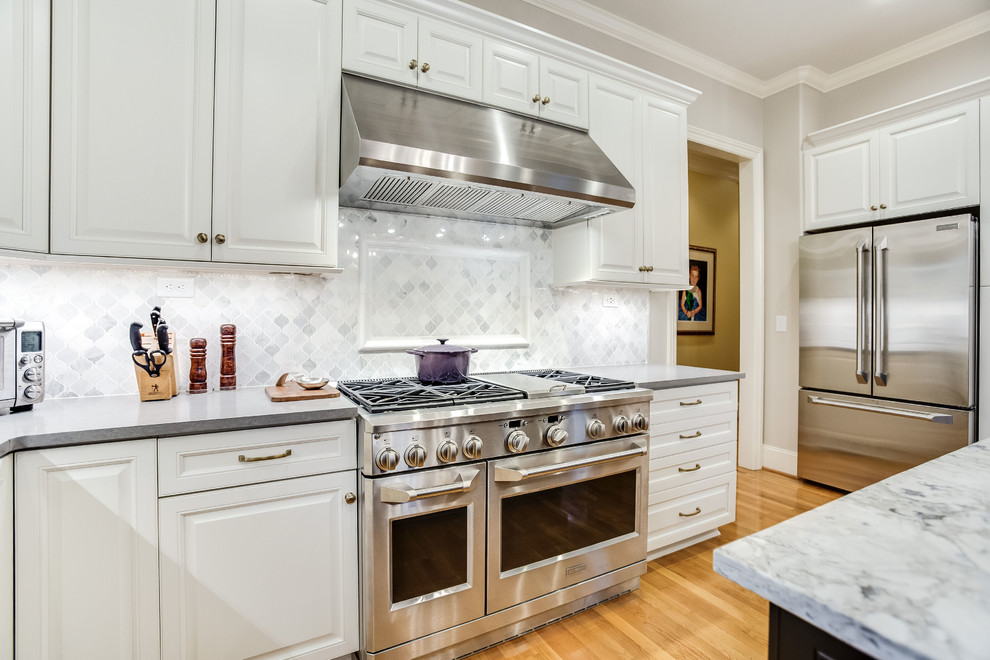 Large transitional u-shaped light wood floor and yellow floor open concept kitchen photo in Birmingham with raised-panel cabinets, white cabinets, marble countertops, white backsplash, marble backsplash, stainless steel appliances, an island and white countertops