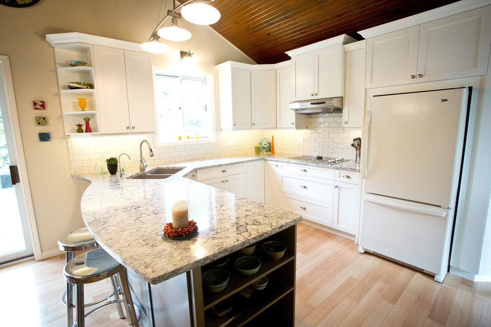 This is an example of a mid-sized transitional u-shaped kitchen in Toronto with an undermount sink, shaker cabinets, white cabinets, granite benchtops, white splashback, subway tile splashback, white appliances, light hardwood floors and a peninsula.