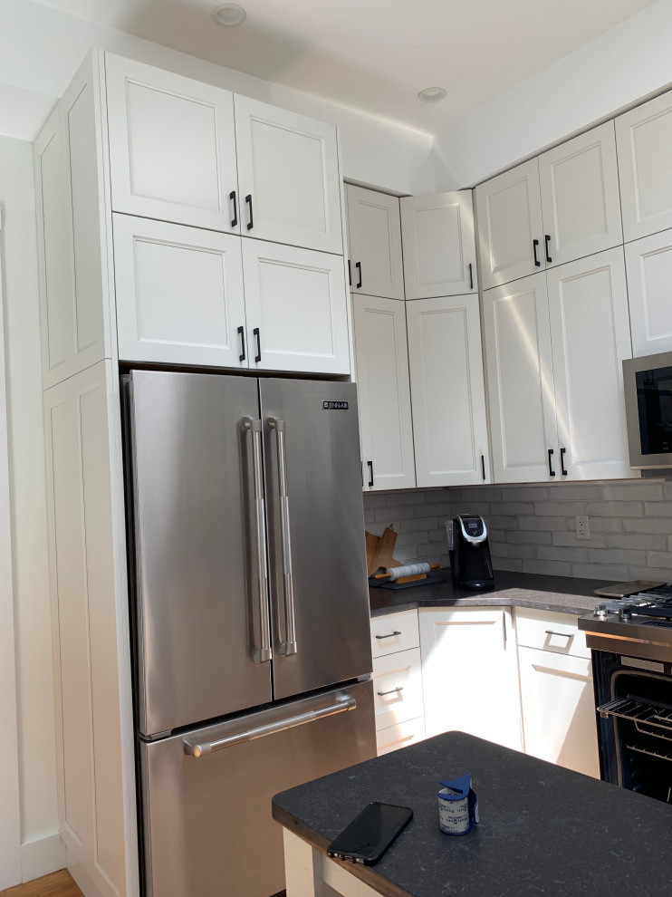 This is an example of a small transitional l-shaped separate kitchen in Boston with an undermount sink, shaker cabinets, white cabinets, quartz benchtops, white splashback, subway tile splashback, stainless steel appliances, medium hardwood floors, a peninsula and black benchtop.