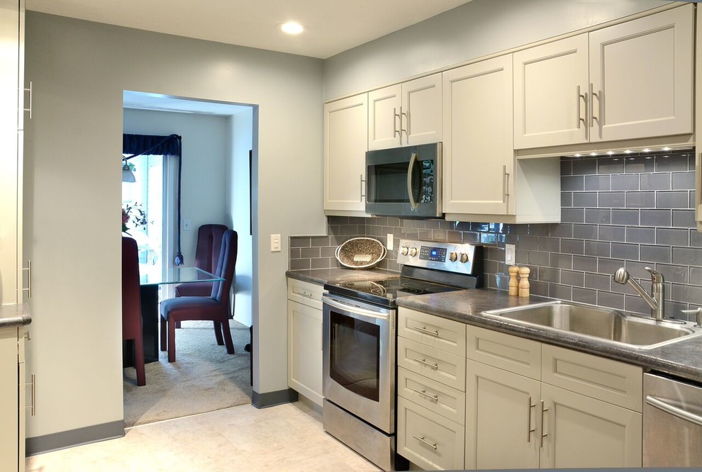 Transitional eat-in kitchen photo in Cleveland with a drop-in sink, yellow cabinets, solid surface countertops, gray backsplash, glass tile backsplash, stainless steel appliances and no island