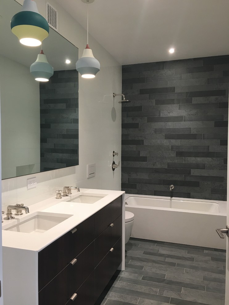 Photo of a large modern kids bathroom in New York with flat-panel cabinets, medium wood cabinets, an undermount tub, a wall-mount toilet, green tile, slate, white walls, slate floors, engineered quartz benchtops, green floor and white benchtops.