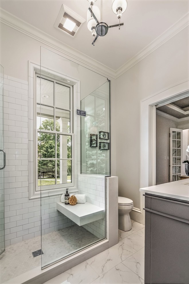 Mid-sized arts and crafts 3/4 bathroom in St Louis with recessed-panel cabinets, grey cabinets, a corner shower, a two-piece toilet, white tile, subway tile, beige walls, marble floors, an undermount sink, solid surface benchtops, white floor and a hinged shower door.