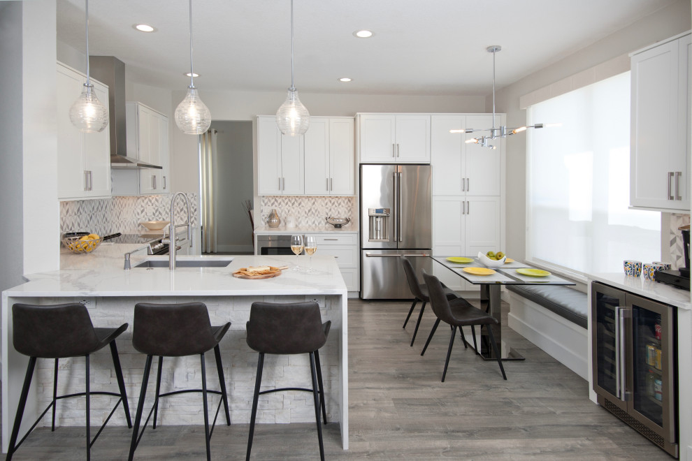 This is an example of a mid-sized transitional l-shaped open plan kitchen in Miami with an undermount sink, shaker cabinets, white cabinets, quartz benchtops, grey splashback, ceramic splashback, stainless steel appliances, laminate floors, grey floor, white benchtop and a peninsula.