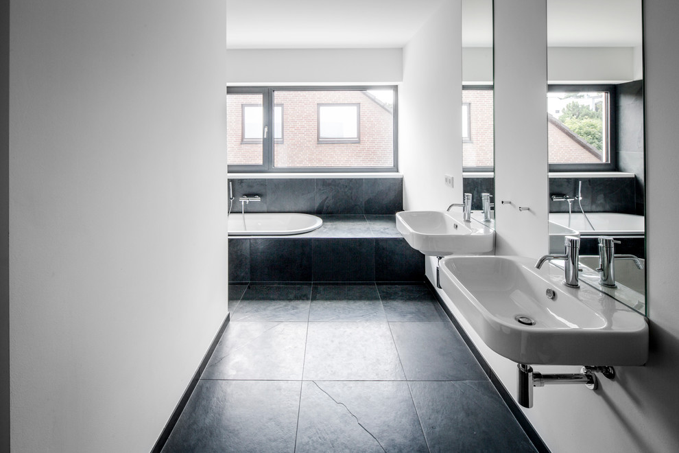 Mid-sized contemporary bathroom in Cologne with a trough sink, a wall-mount sink, a drop-in tub, gray tile, white walls, stone tile and slate floors.