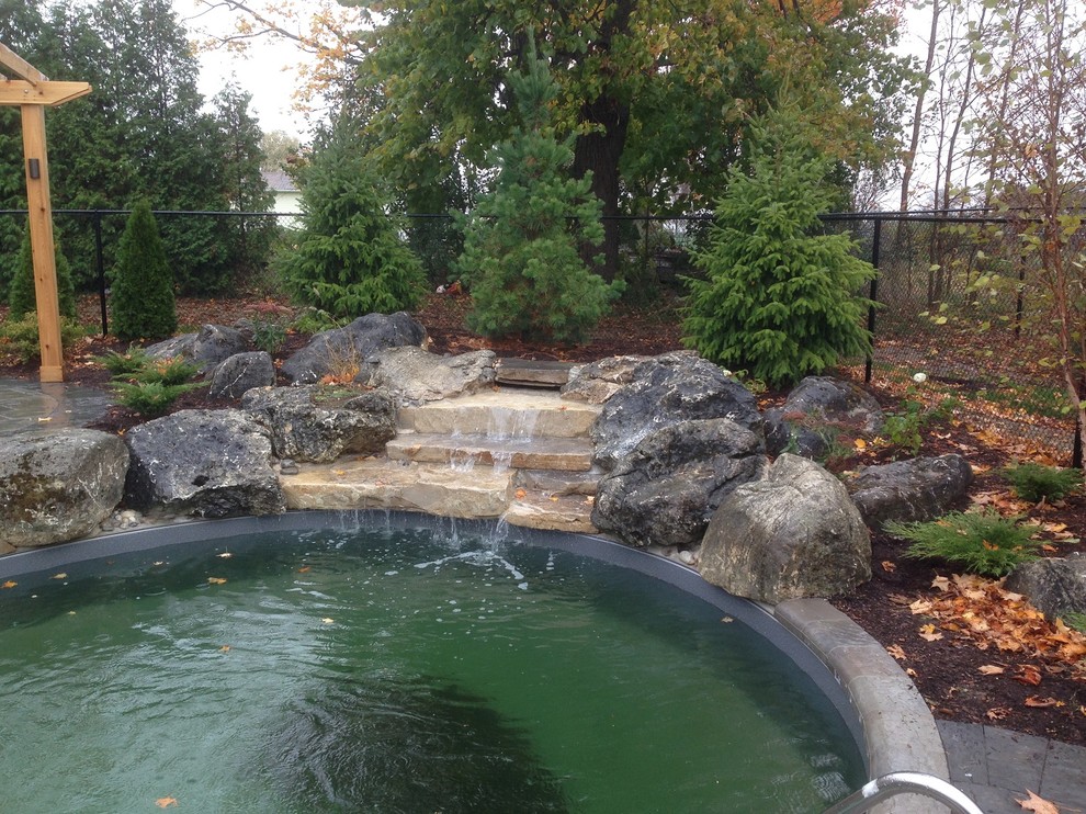 Mid-sized tropical backyard custom-shaped pool in Toronto with natural stone pavers and a water feature.