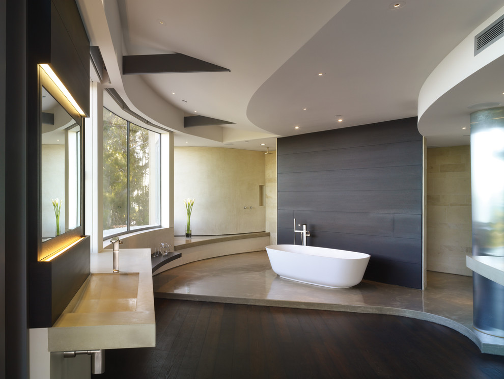 This is an example of a mid-sized contemporary master bathroom in Los Angeles with concrete benchtops, a freestanding tub, an integrated sink, flat-panel cabinets, dark wood cabinets, an open shower, beige tile, stone tile, white walls, dark hardwood floors and an open shower.