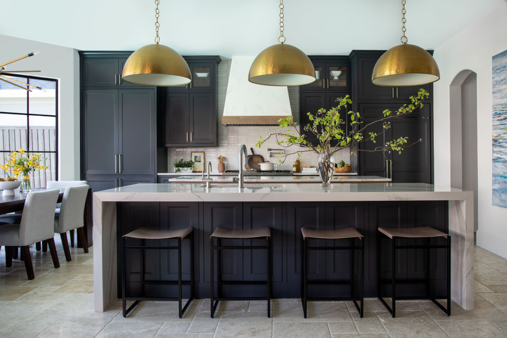 Design ideas for a large classic open plan kitchen in Houston with a belfast sink, shaker cabinets, black cabinets, composite countertops, white splashback, metro tiled splashback, integrated appliances, travertine flooring, multiple islands, beige floors and white worktops.