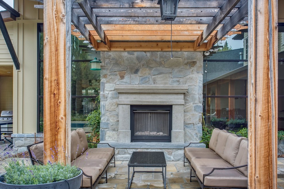 Large industrial courtyard patio in Calgary with with fireplace, natural stone pavers and a pergola.