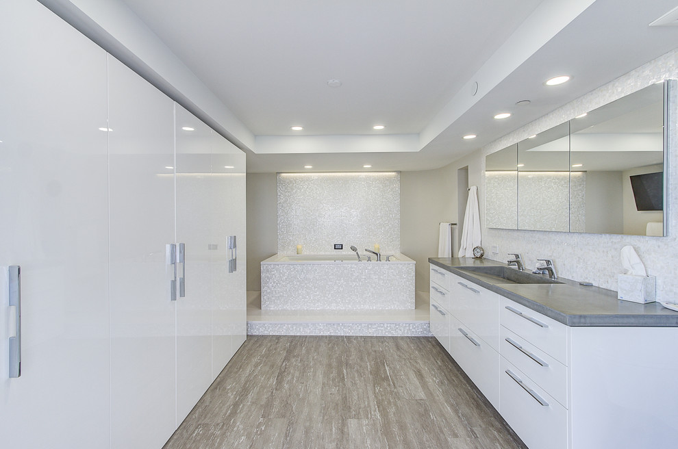 Inspiration for a mid-sized modern master bathroom in Other with flat-panel cabinets, white cabinets, an undermount tub, gray tile, stone slab, grey walls, medium hardwood floors, a trough sink, concrete benchtops, brown floor and grey benchtops.