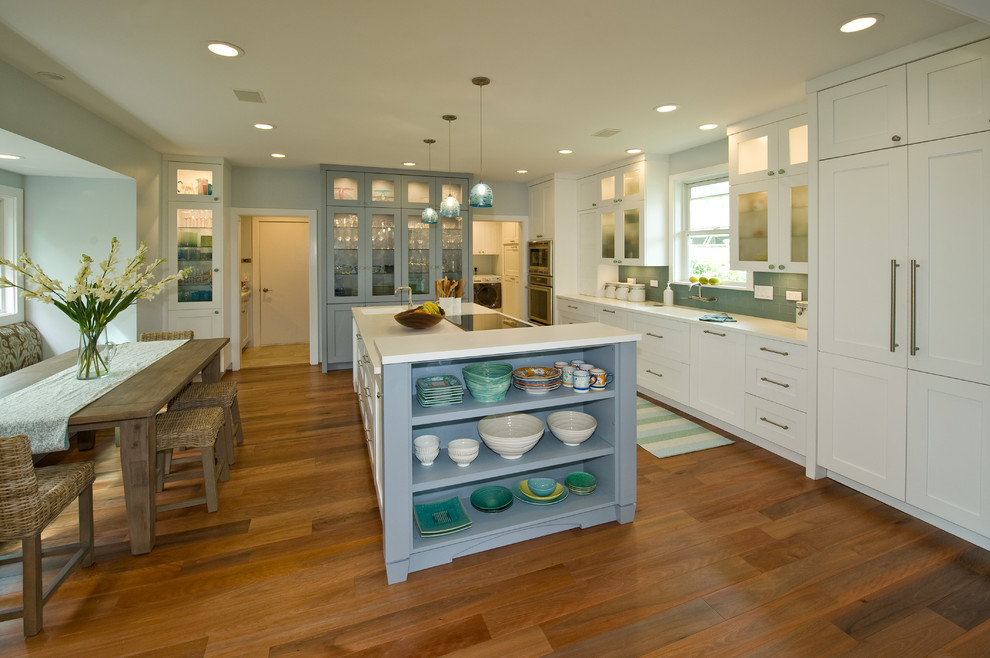 This is an example of a tropical kitchen pantry in Hawaii with an integrated sink, shaker cabinets, white cabinets, solid surface benchtops, blue splashback, glass tile splashback, panelled appliances and with island.