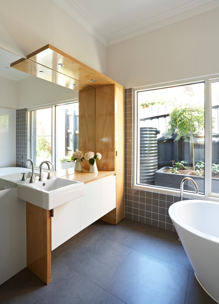 Design ideas for a large contemporary master bathroom in Melbourne with flat-panel cabinets, wood benchtops, a freestanding tub, an alcove shower, a one-piece toilet, gray tile, porcelain tile, white walls, porcelain floors, white cabinets and a console sink.