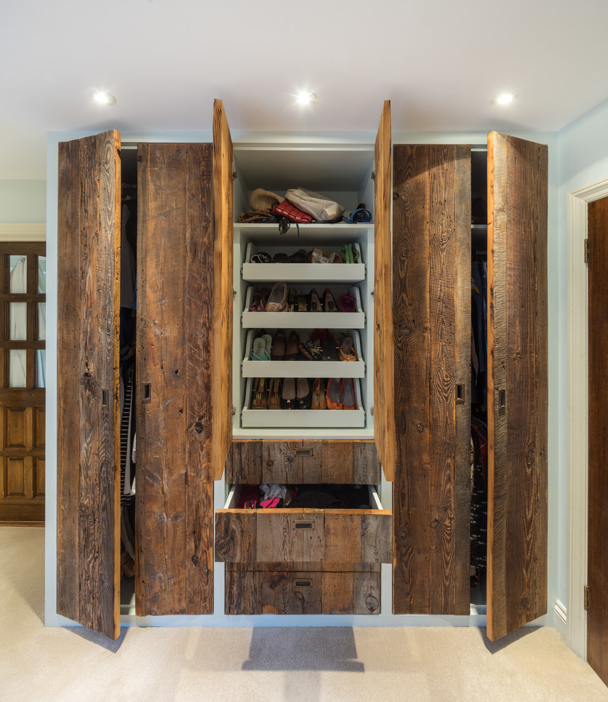 This is an example of a mid-sized traditional gender-neutral built-in wardrobe in London with flat-panel cabinets, medium wood cabinets, carpet and beige floor.