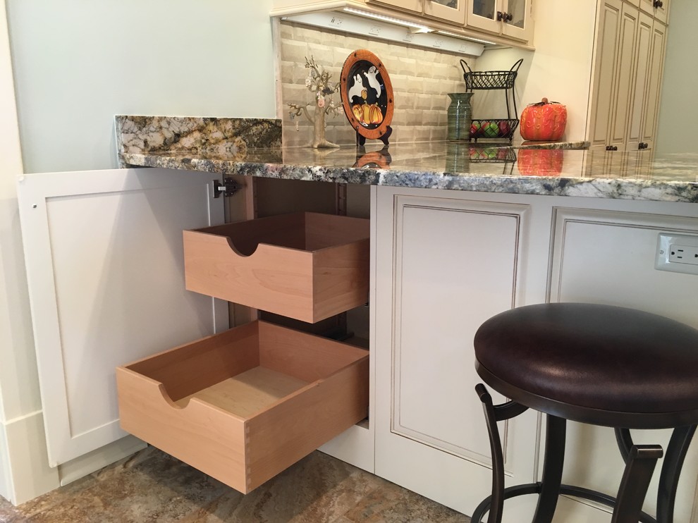 Large transitional galley porcelain tile enclosed kitchen photo with an undermount sink, raised-panel cabinets, distressed cabinets, granite countertops, beige backsplash, stone tile backsplash, stainless steel appliances and a peninsula