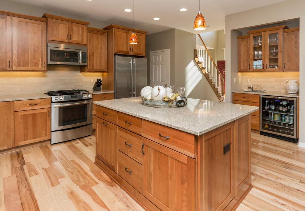Mid-sized transitional l-shaped light wood floor open concept kitchen photo with an undermount sink, recessed-panel cabinets, medium tone wood cabinets, quartz countertops, beige backsplash, stone tile backsplash, stainless steel appliances and an island