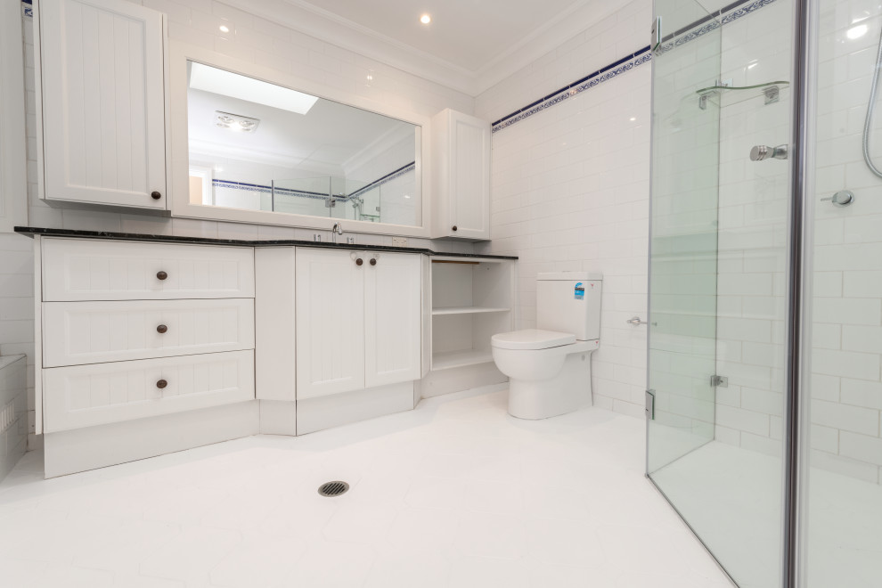 Example of a small classic white tile and ceramic tile ceramic tile, white floor and single-sink bathroom design in Sydney with recessed-panel cabinets, white cabinets, a two-piece toilet, white walls, an undermount sink, solid surface countertops, a hinged shower door, black countertops and a freestanding vanity
