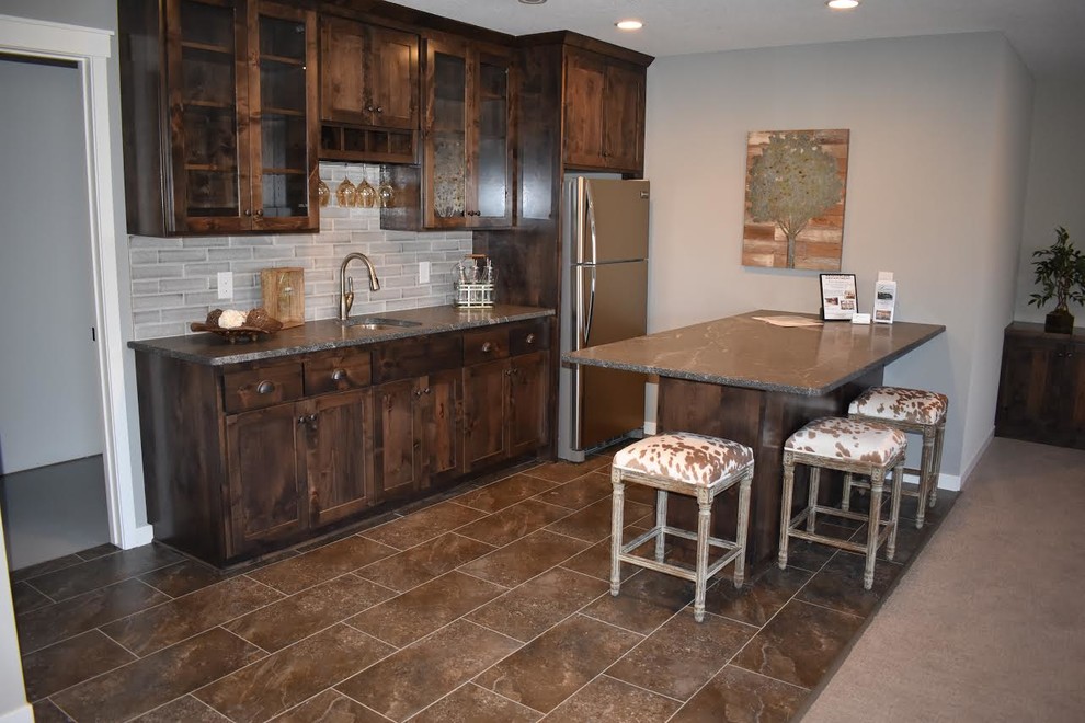 Photo of a mid-sized country single-wall seated home bar in Minneapolis with an undermount sink, shaker cabinets, dark wood cabinets, quartz benchtops, grey splashback, porcelain splashback, porcelain floors and brown floor.