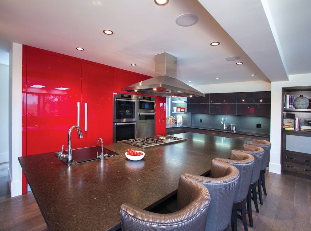 Inspiration for a large modern l-shaped eat-in kitchen in Calgary with a double-bowl sink, glass-front cabinets, red cabinets, granite benchtops, grey splashback, glass tile splashback, stainless steel appliances, dark hardwood floors and with island.