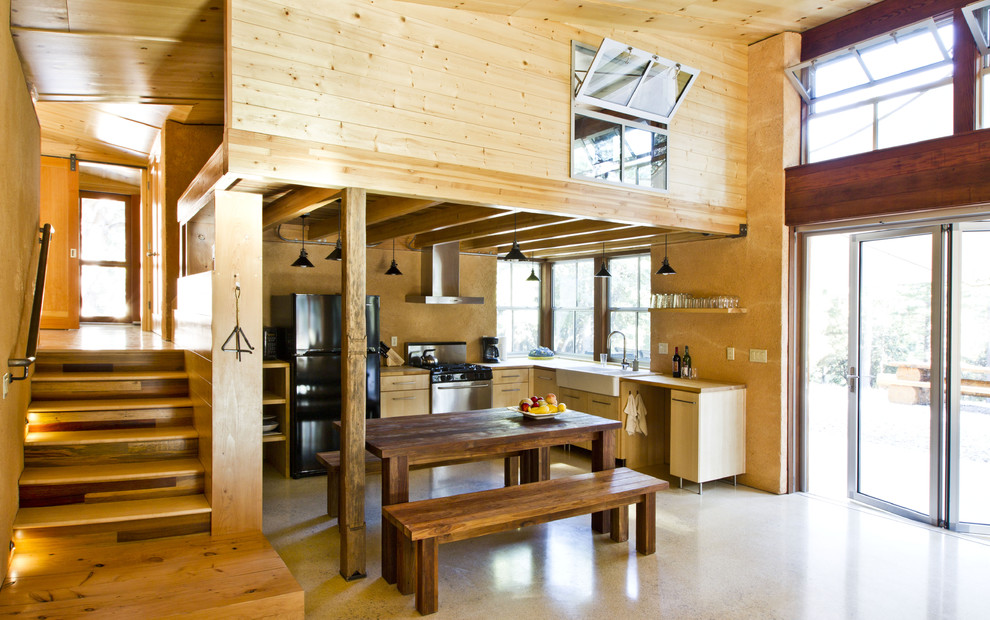 This is an example of a small country l-shaped eat-in kitchen in Sacramento with a farmhouse sink, flat-panel cabinets, light wood cabinets, black appliances, wood benchtops, concrete floors and no island.