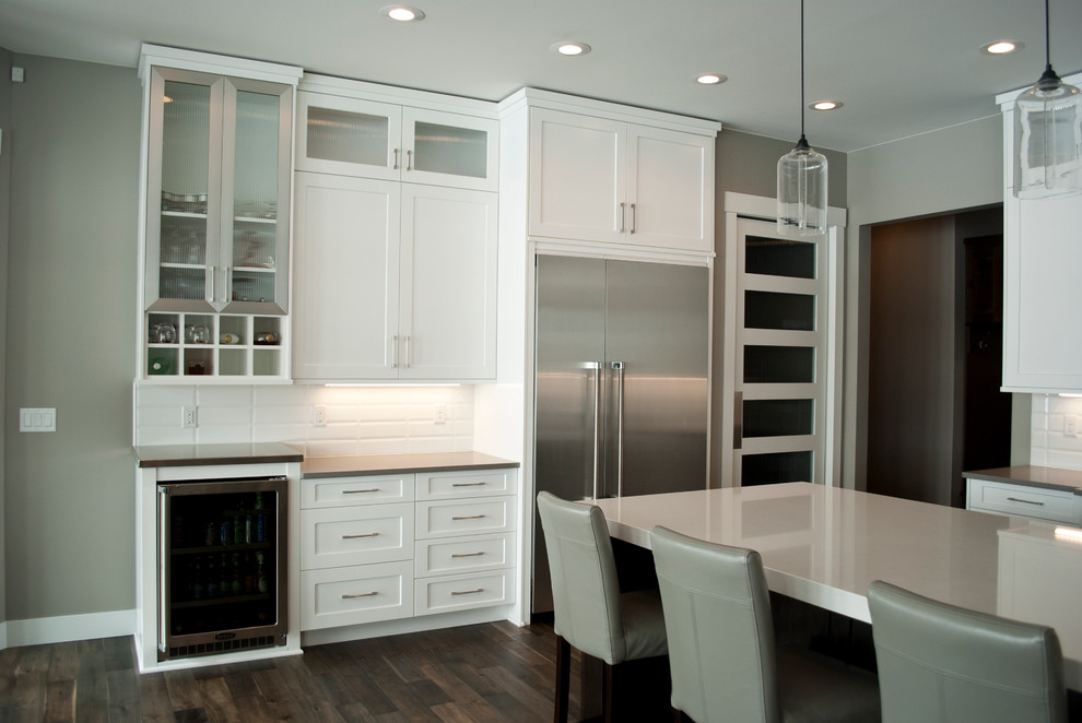 Example of a transitional kitchen design with recessed-panel cabinets, white cabinets, quartz countertops, white backsplash, stainless steel appliances and an island