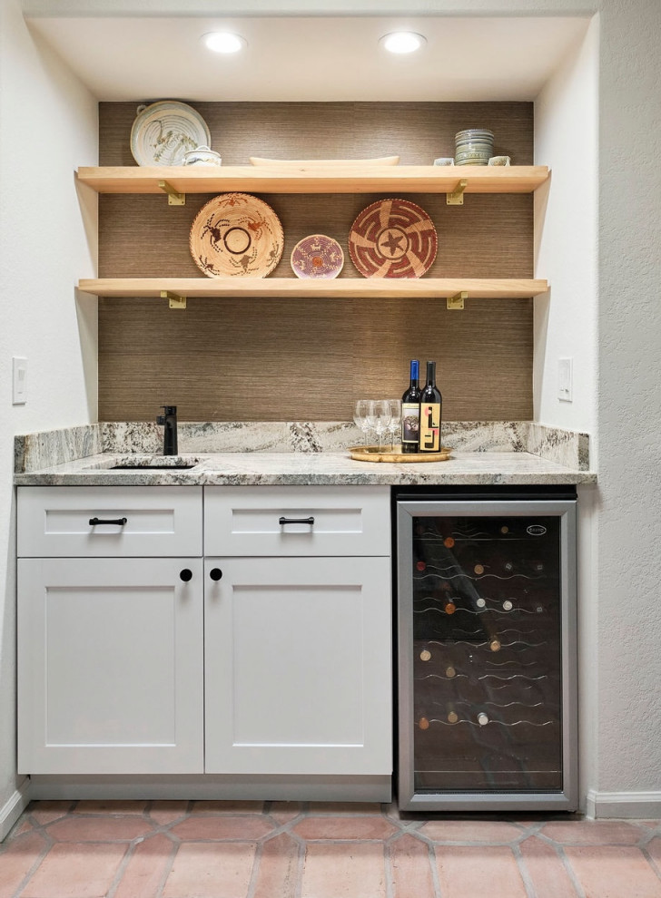 Photo of a small transitional single-wall wet bar in Phoenix with an undermount sink, shaker cabinets, white cabinets, granite benchtops, granite splashback, terra-cotta floors and multi-coloured benchtop.