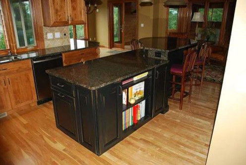 Mid-sized transitional l-shaped light wood floor kitchen photo in Milwaukee with recessed-panel cabinets, black cabinets, granite countertops, beige backsplash, stone tile backsplash, stainless steel appliances and an island