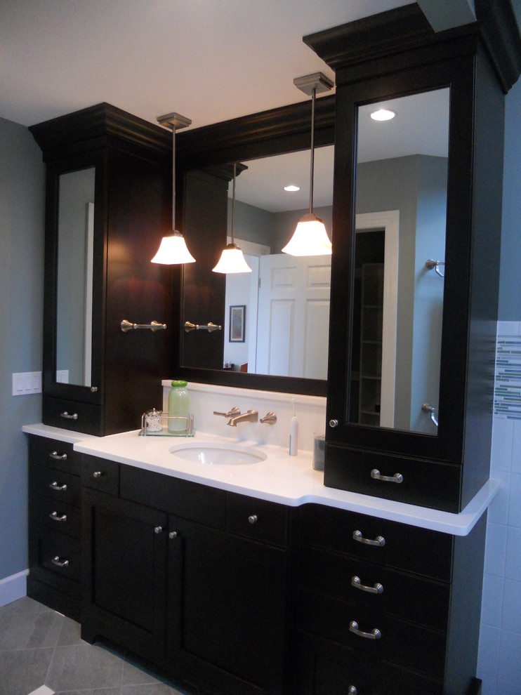 Example of a large transitional master gray tile and stone tile ceramic tile corner bathtub design with an undermount sink, recessed-panel cabinets, dark wood cabinets, quartz countertops, a two-piece toilet and gray walls