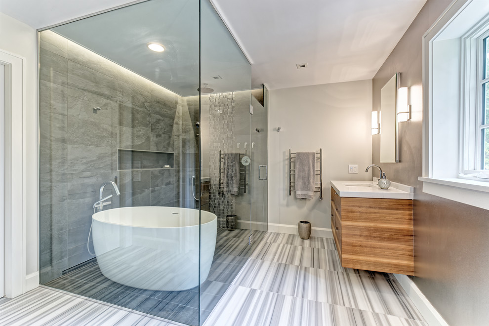 Inspiration for a mid-sized transitional master gray tile and porcelain tile marble floor and gray floor freestanding bathtub remodel in New York with furniture-like cabinets, medium tone wood cabinets, a wall-mount toilet, gray walls, an undermount sink, quartz countertops, a hinged shower door and white countertops