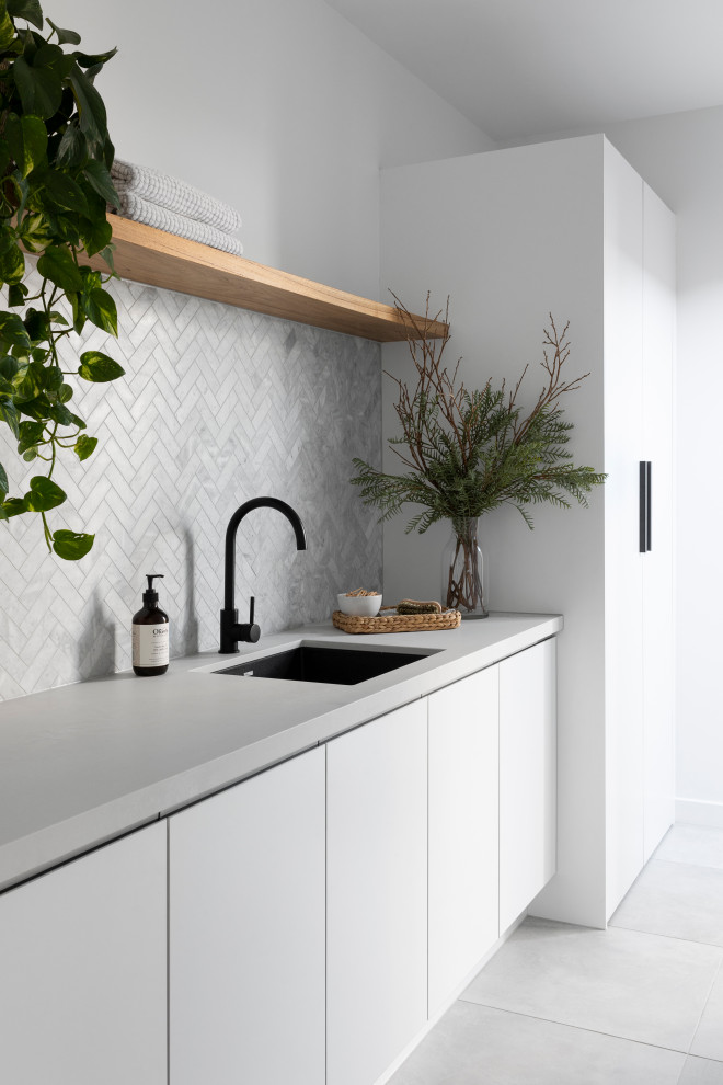Inspiration for a large contemporary galley dedicated laundry room in Melbourne with an undermount sink, flat-panel cabinets, white cabinets, quartz benchtops, grey splashback, ceramic splashback, white walls, ceramic floors, grey floor and grey benchtop.