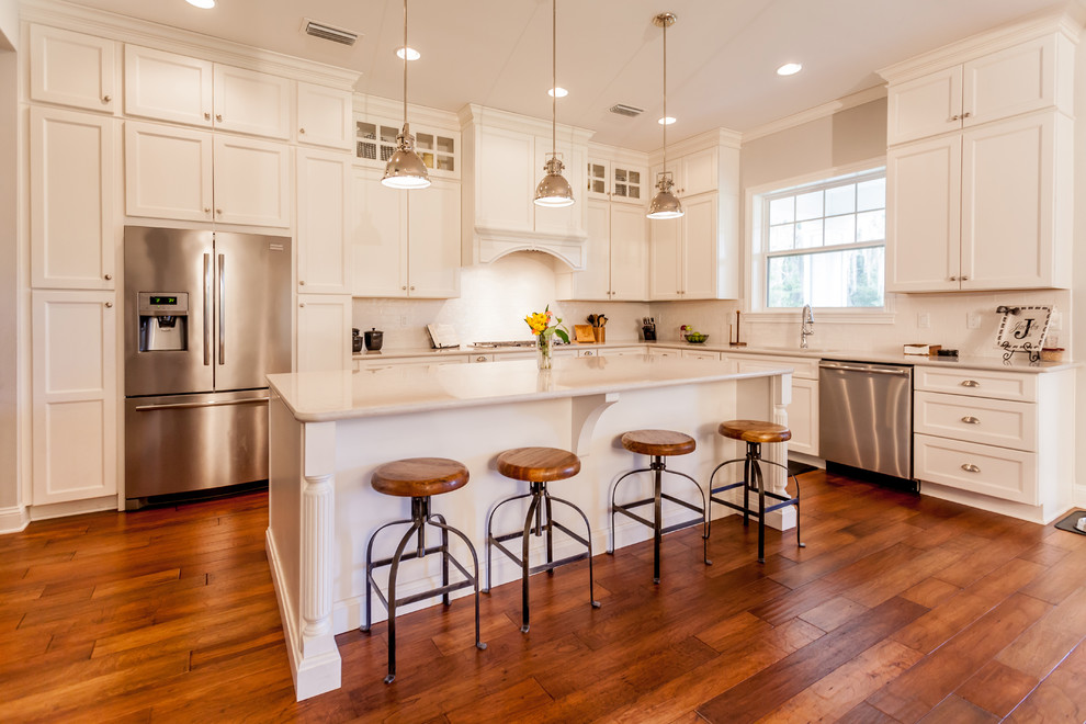 This is an example of a large country l-shaped open plan kitchen in Jacksonville with shaker cabinets, white cabinets, white splashback, stainless steel appliances, medium hardwood floors, with island, an undermount sink, granite benchtops, subway tile splashback and brown floor.