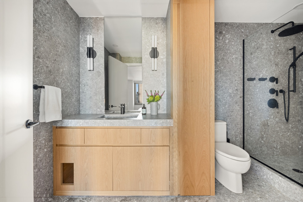 Foto på ett mellanstort funkis grå en-suite badrum, med släta luckor, en dusch i en alkov, en toalettstol med separat cisternkåpa, grå kakel, porslinskakel, grå väggar, klinkergolv i porslin, ett integrerad handfat, grått golv, skåp i ljust trä och bänkskiva i terrazo