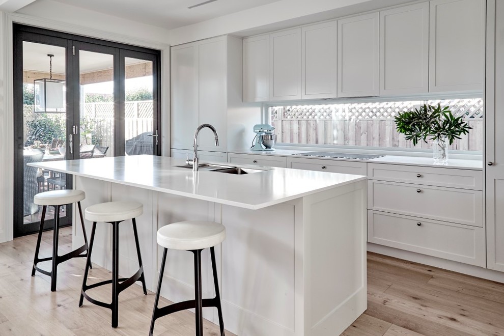 This is an example of a mid-sized transitional galley eat-in kitchen in Sydney with shaker cabinets, beige cabinets, quartz benchtops, glass sheet splashback, stainless steel appliances, light hardwood floors, with island, an undermount sink and white benchtop.