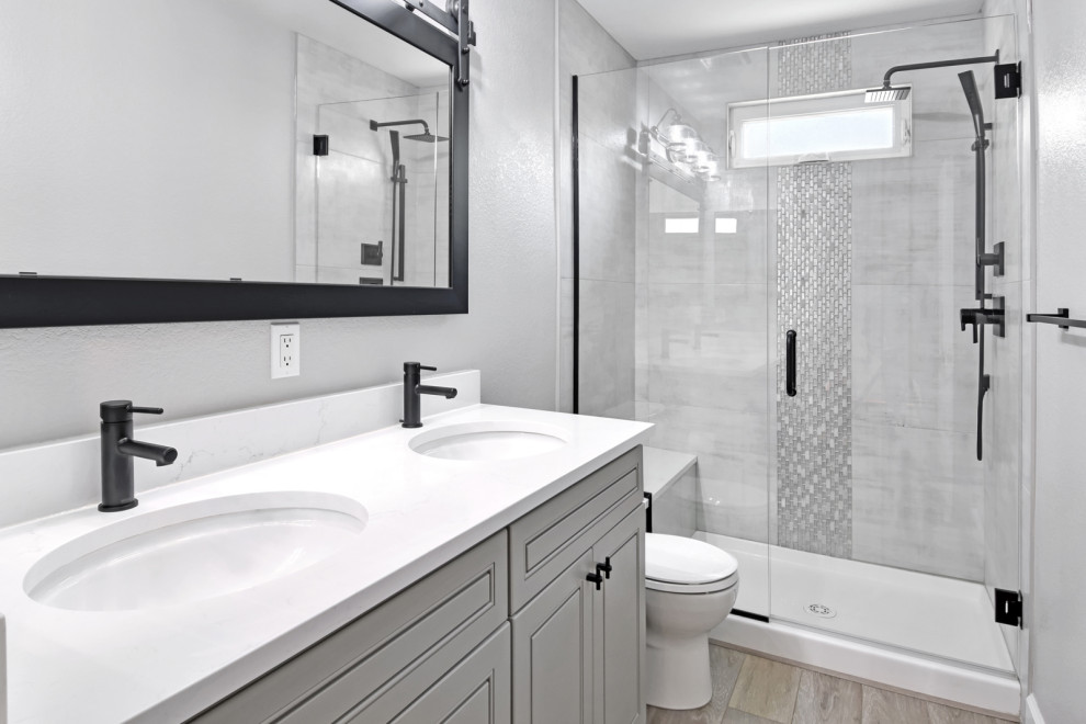 Idées déco pour une salle de bain moderne de taille moyenne avec un placard à porte affleurante, des portes de placard grises, un carrelage gris, des carreaux de porcelaine, un mur blanc, sol en stratifié, un lavabo encastré, un plan de toilette en quartz, un sol marron, une cabine de douche à porte battante, un plan de toilette blanc, une niche, meuble double vasque et meuble-lavabo sur pied.