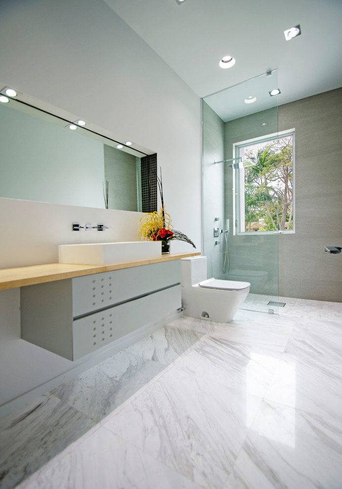 Inspiration for a mid-sized modern 3/4 bathroom in Miami with grey cabinets, an open shower, a one-piece toilet, gray tile, white walls, wood benchtops, a vessel sink, marble floors, flat-panel cabinets and an open shower.